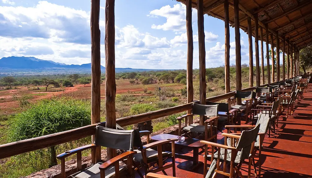 The long open-air viewing terrace of Kilaguni Serena Safari Lodge inside Tsavo West National Park, its timber pillars framing the red volcanic plain and the hills beyond